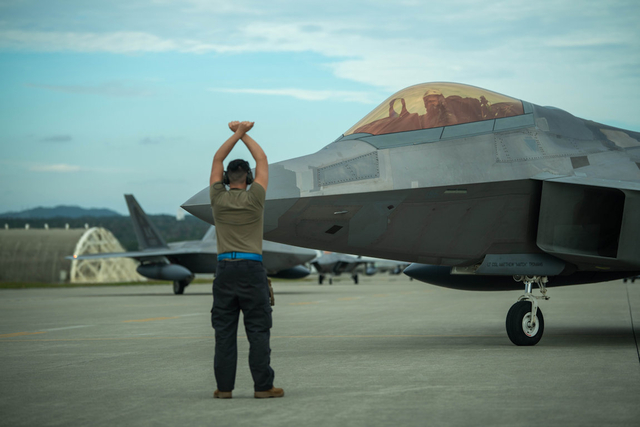 A U.S. Air Force Airman marshals a F-22A Raptor assigned to the 3rd Wing into position at Kadena Air Base, Japan, Nov. 4, 2022. The deployment of newer and more advanced aircraft at Kadena exemplifies Department of Defense's continued commitment to enhancing our posture while building on the strong foundation of our Alliances with Japan. (U.S. Air Force photo by Airman 1st Class Alexis Redin)